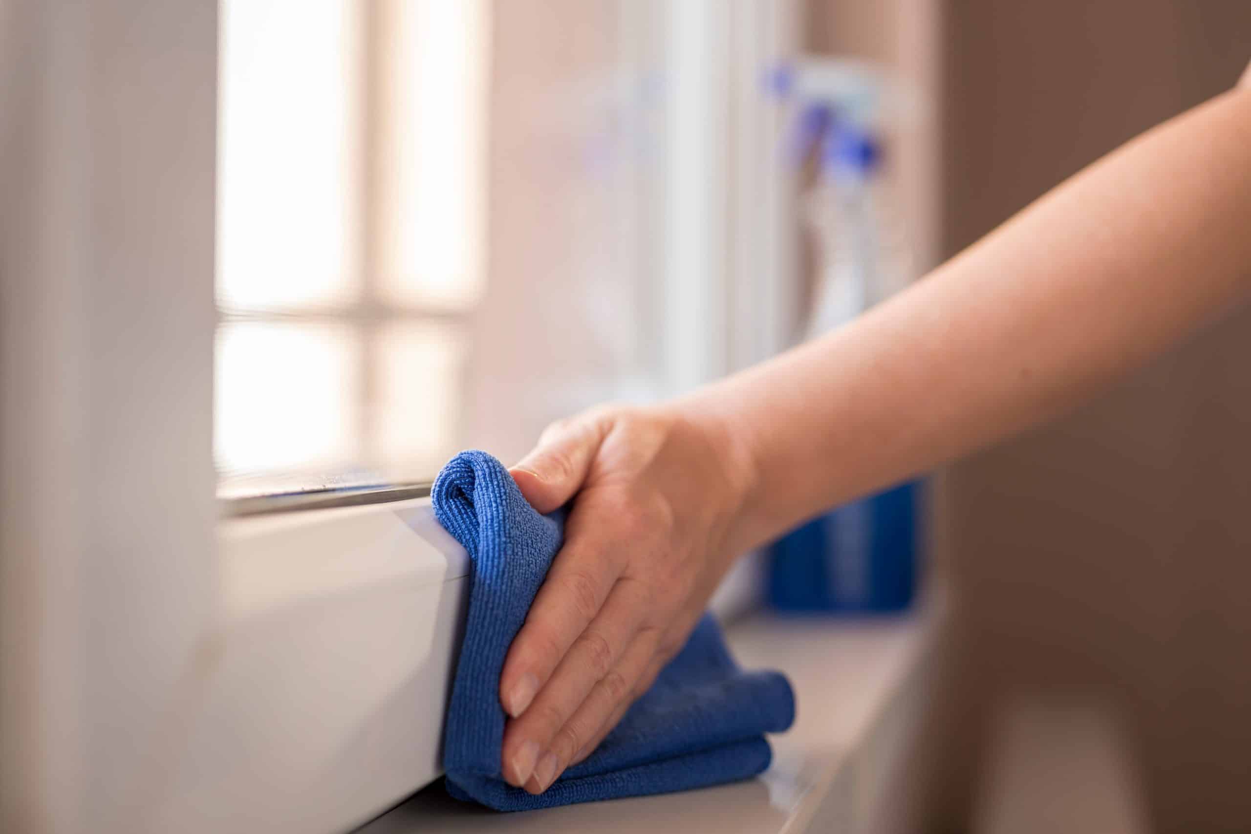 Detail of Ayrshire woman's hands wiping new uPVC windows from Andrew Wright Windows with a cleanser spray and a microfibre cloth.